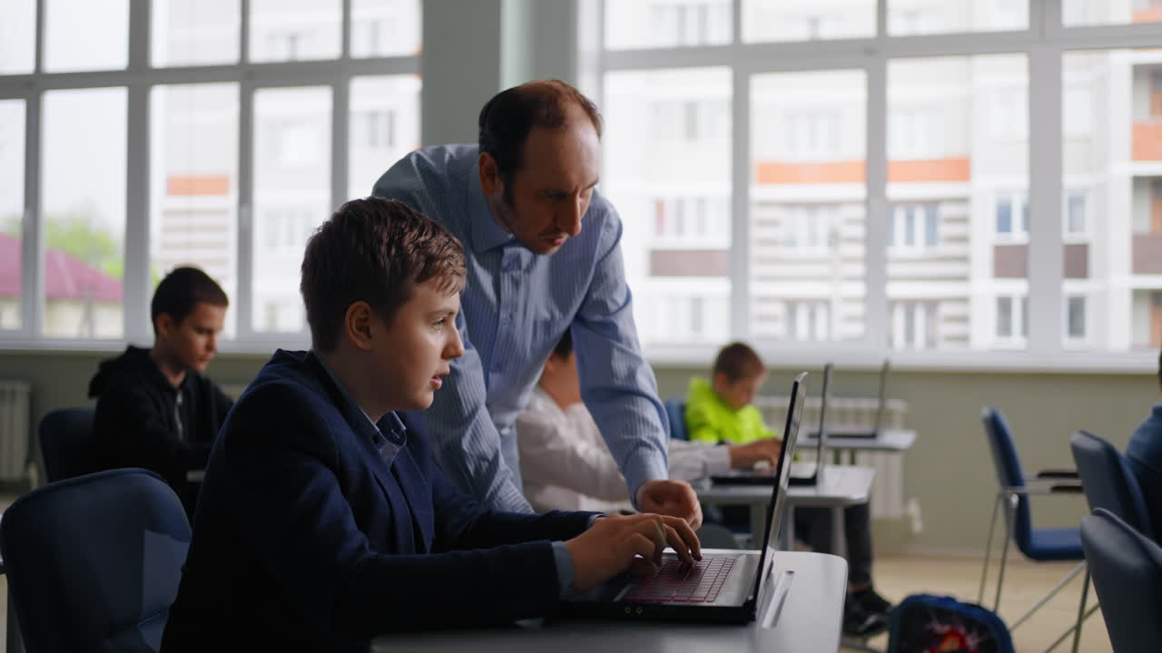Teacher assisting student with laptop in classroom