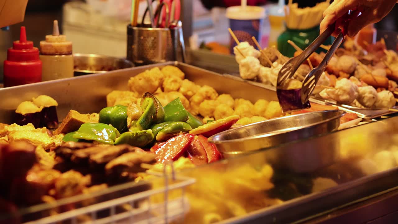 vendedor preparando una variedad de comida callejera con pinzas