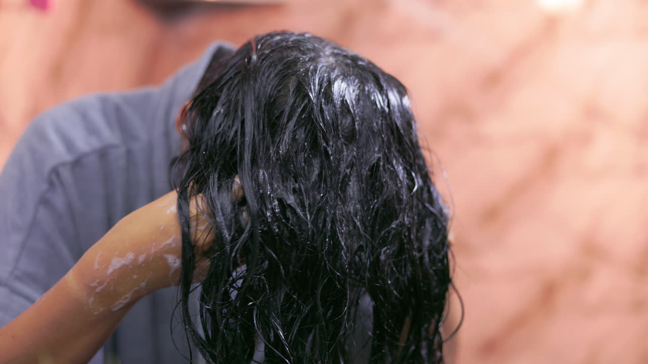 Una donna che si lava i capelli con lo shampoo durante la sua routine quotidiana di cura dei capelli.