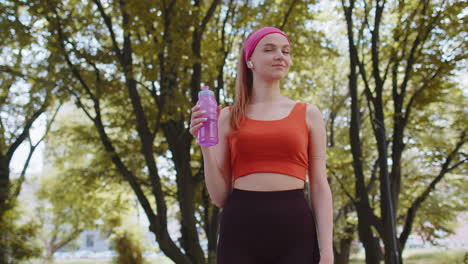 athletic fit sport runner adult girl drinking water from bottle after training exercising in park