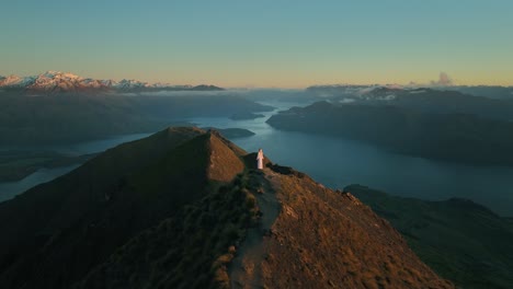 fairytale scene of woman in white dress standing on mountain peak at dawn