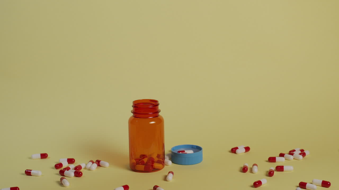 Slow motion wide shot of pills as they fall vertically towards an open pill bottle and lid