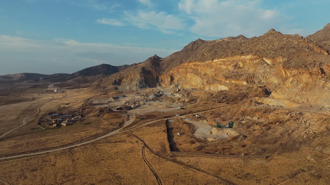 Stone quarry aerial wide shot at the base of old mountains , sunny day blue sky