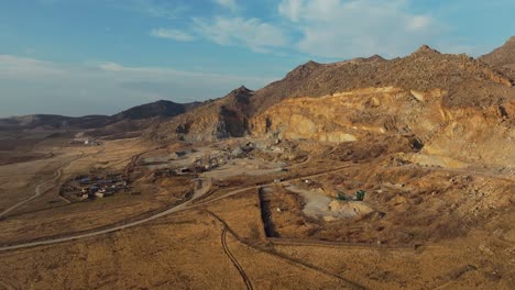 stone quarry aerial wide shot at the base of old mountains , sunny day blue sky