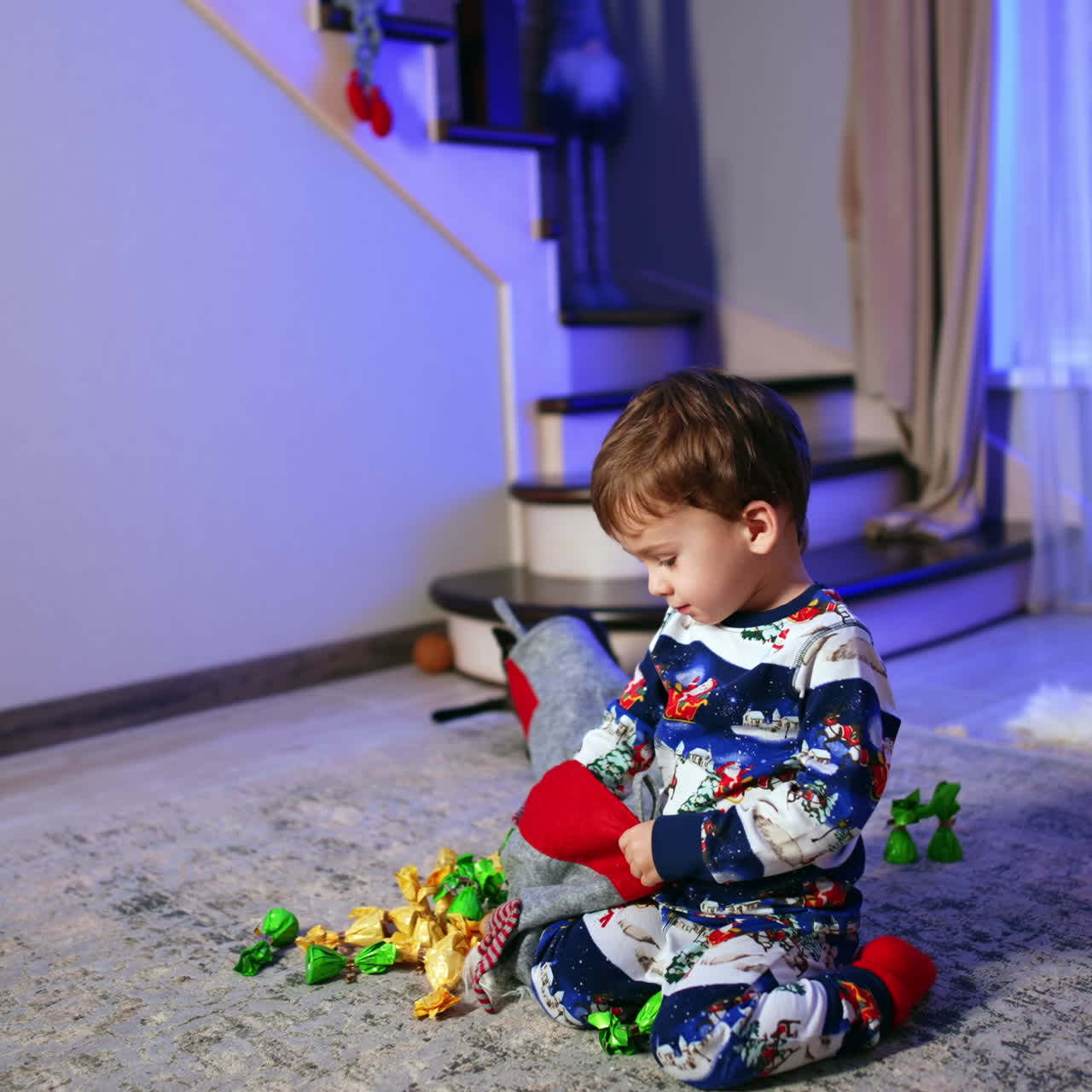 Getting Christmas presents from stockings. Baby boy sitting on the floor pulls the candies out of stocking.