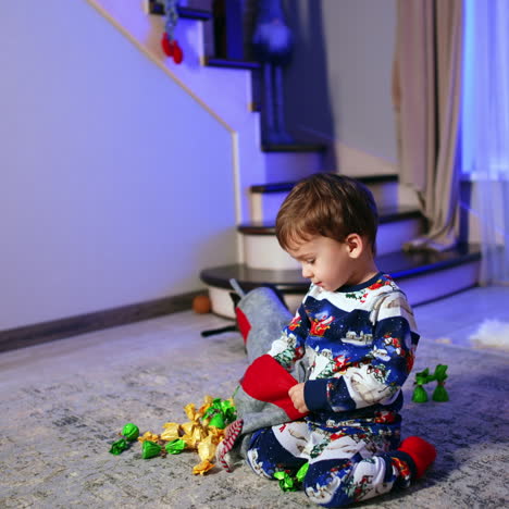 getting christmas presents from stockings. baby boy sitting on the floor pulls the candies out of stocking.