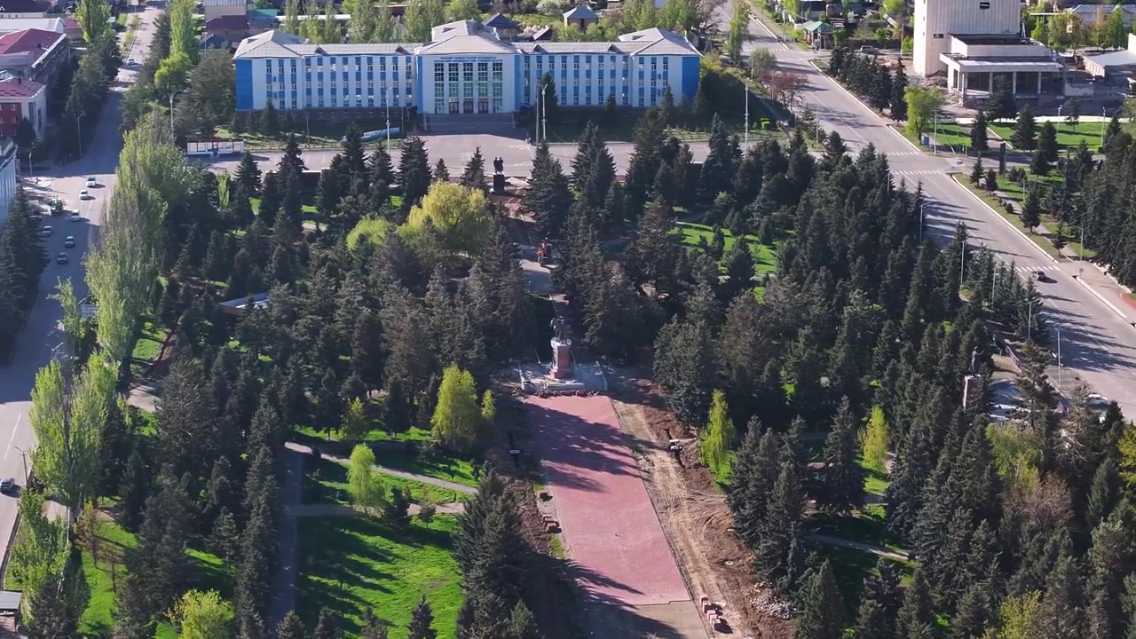Parco pubblico della città di Karakol con statua simbolo ed edificio universitario, paesaggio urbano del Kirghizistan ripreso con drone