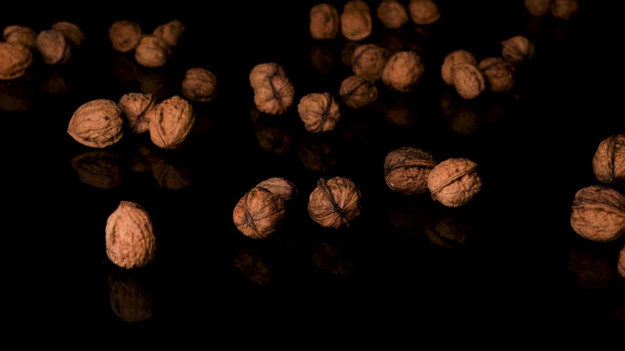 Walnuts in the shell falling on the black reflective surface in slow motion