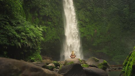 woman in zen sukhasana easy pose with mighty water rush from nungnung waterfall