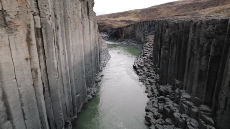 aerial dolly past basalt columns of studlagil canyon, iceland, above river