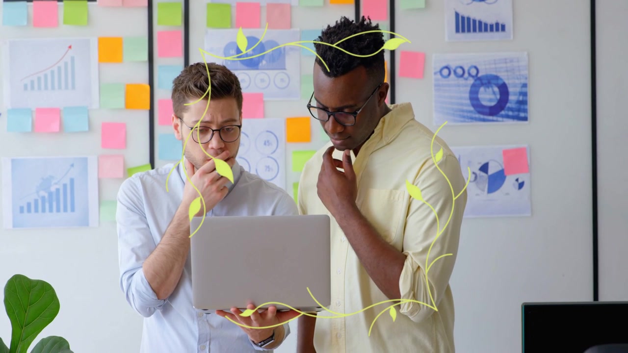 Two men in business left holding laptop pointing and causing floral overlay while reviewing charts