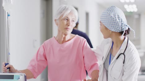 video de una doctora diversa y una paciente mayor hablando en el pasillo del hospital