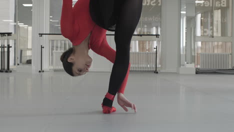 cool shot of a ballerina stretching down while standing on one leg