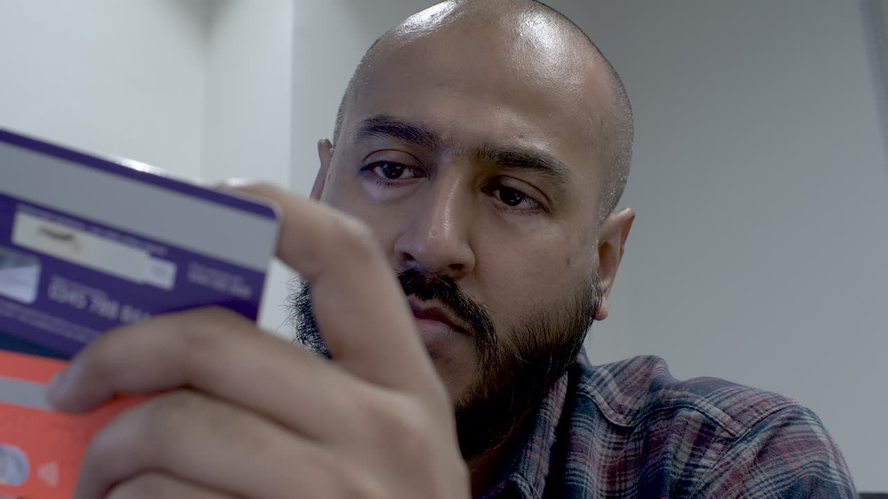 un primer plano de un hombre indio revisando cuidadosamente los detalles de sus 2 tarjetas de crédito, calculando qué tarjeta tiene suficientes fondos disponibles para usar en una compra en línea