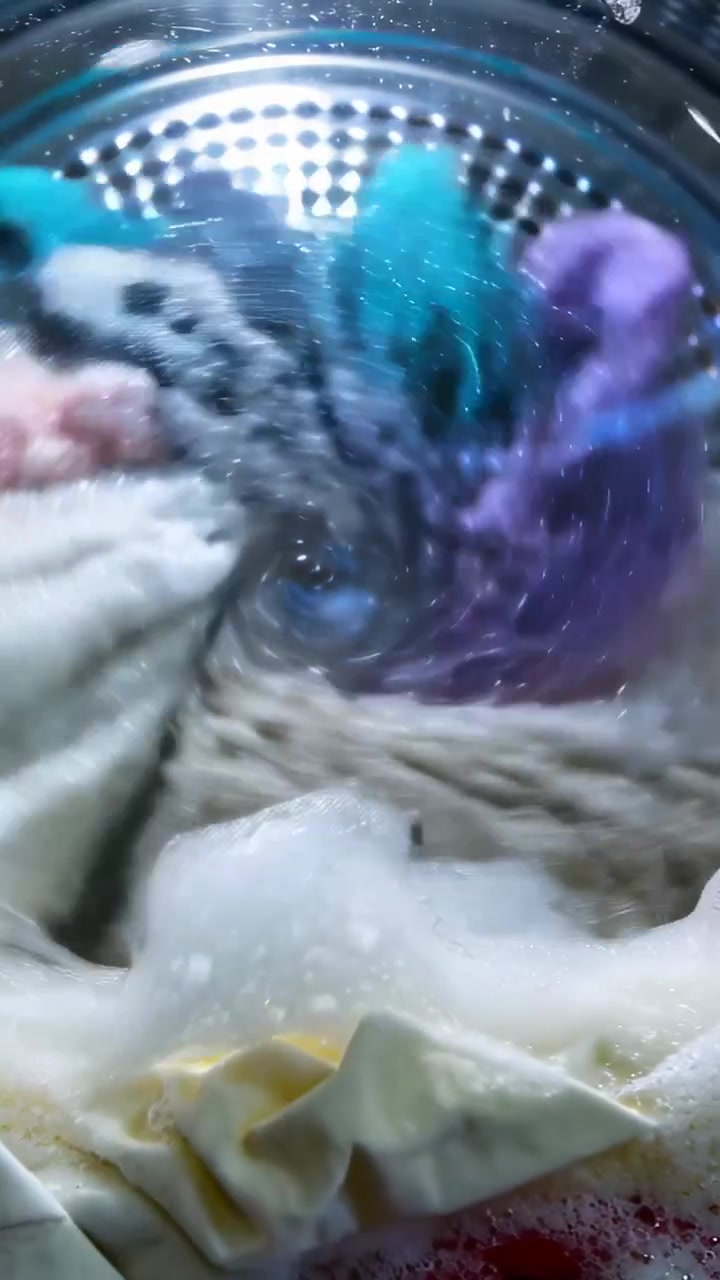 Vertical video: Starting wash cycle, vivid garments spinning inside front-load drum in laundry room