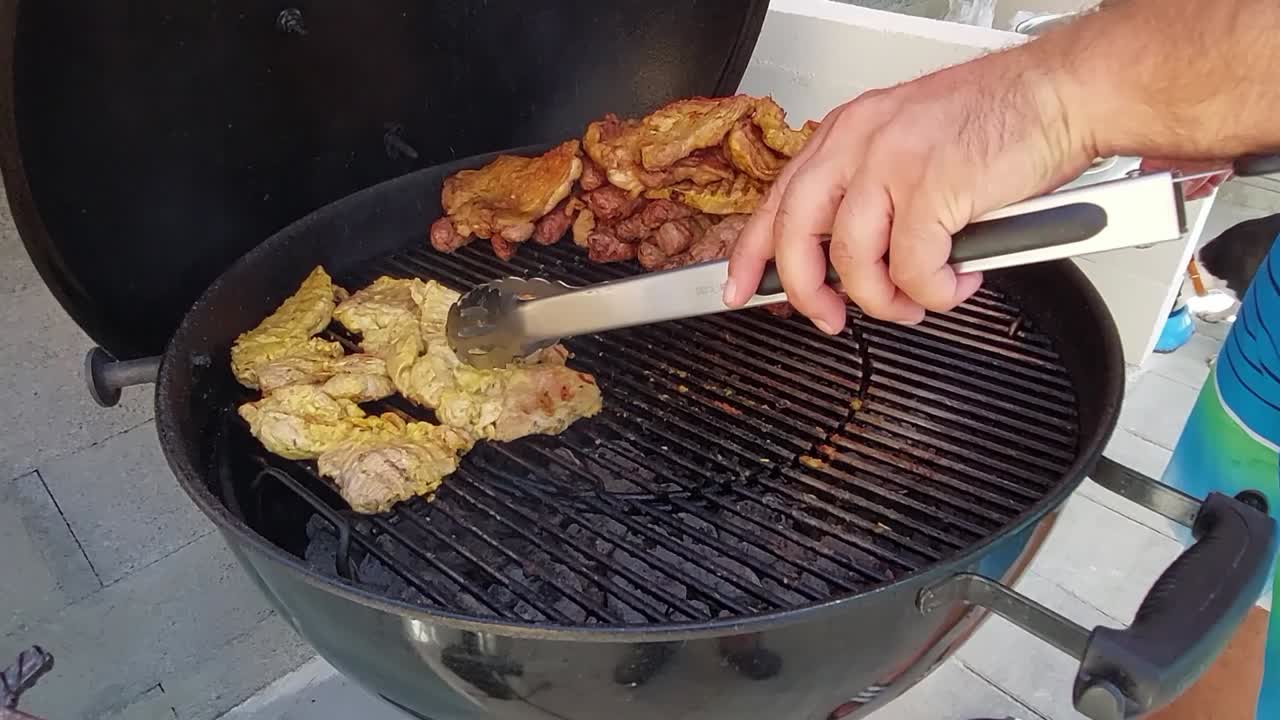 철제 집게를 가진 남자가 숯불 바비큐에 고기를 놓고 버터를 바른 빵을 얹고 있다