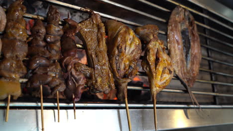 vertical of butterflied boneless milkfish and barbecue on sticks grilling over charcoal. closeup