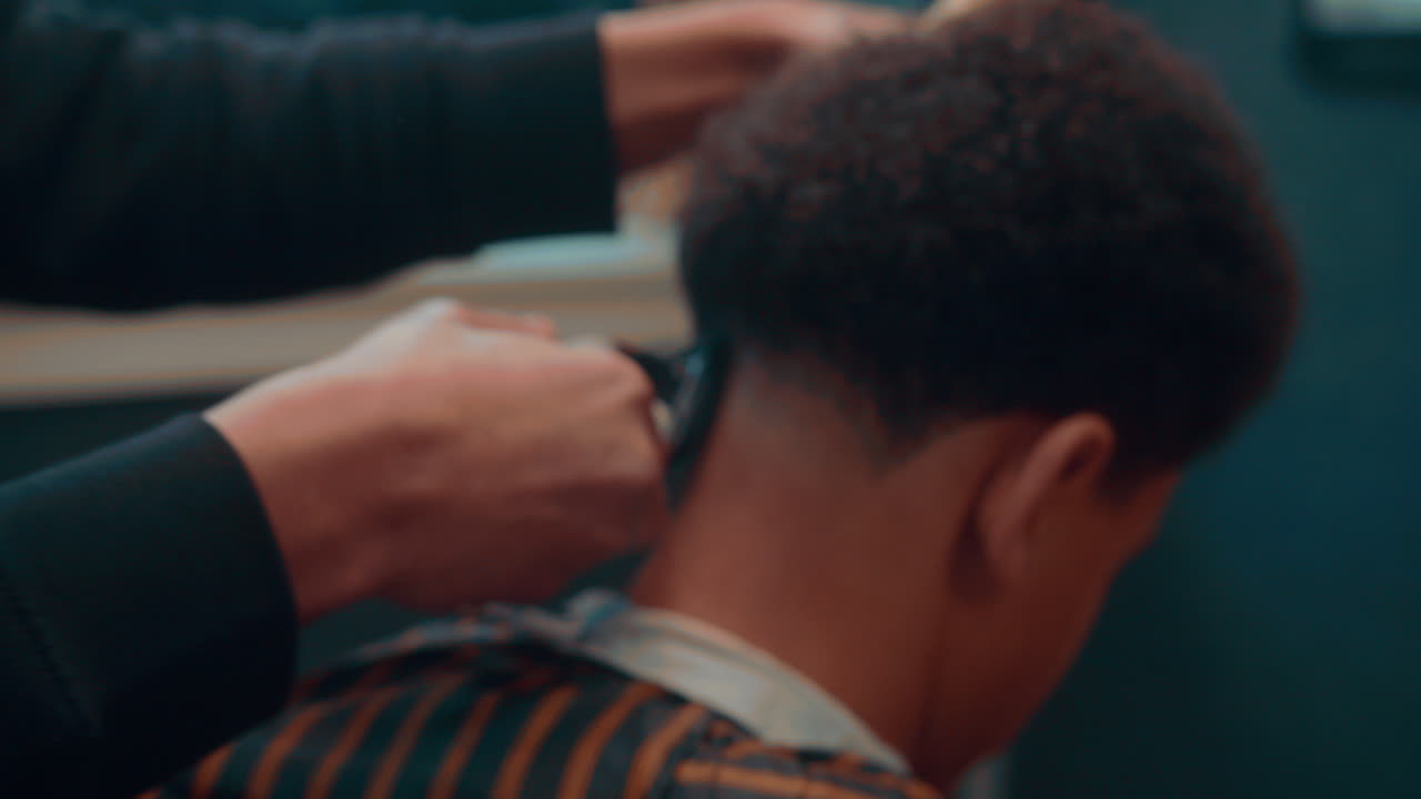 increíble toma en cámara lenta de una toma larga de un corte de pelo por un barbero profesional en una barbería con un movimiento suave de una navaja de afeitar a un joven afro durante la tarde