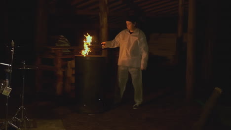 person lighting a fire in a dark rustic venue with drums.