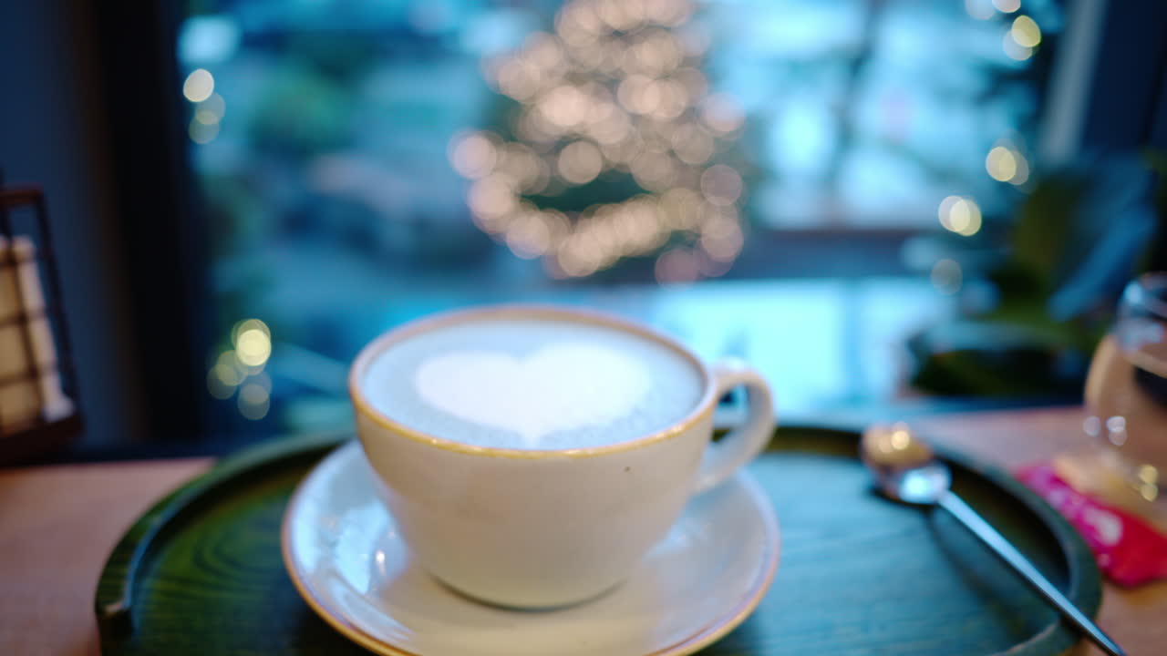 Cup of coffee with foam latte art in heart shape. Christmas tree on background