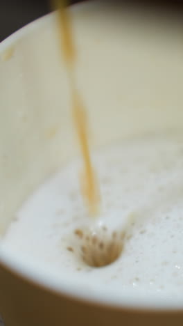 café vertiendo en una taza de una máquina de café. el video captura la vista detallada de la corriente de café mezclándose con la leche espumosa en la taza, destacando el proceso de preparación del café