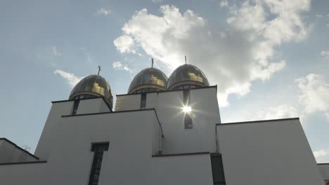 a white church with gold domes against a blue sky with clouds