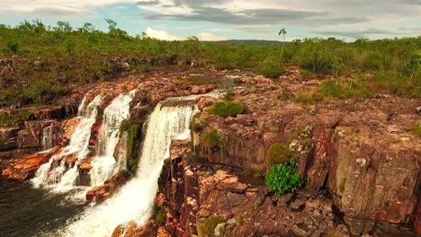 Drone-shot-pulling-back-over-a-river-flowing-into-a-small-waterfall-on-a-rocky-cliff