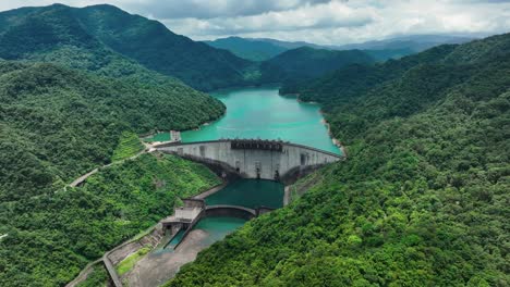 aerial backwards shot of feitsui dam surrounded by tropical mountain landscape during cloudy day