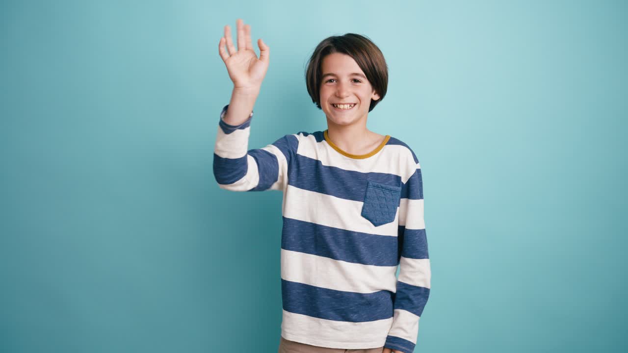 Giovane ragazzo felice che saluta con le mani e sorride alla fotocamera.