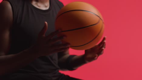 toma de estudio de cerca de un jugador de baloncesto masculino lanzando la pelota de mano en mano contra un fondo rojo 1