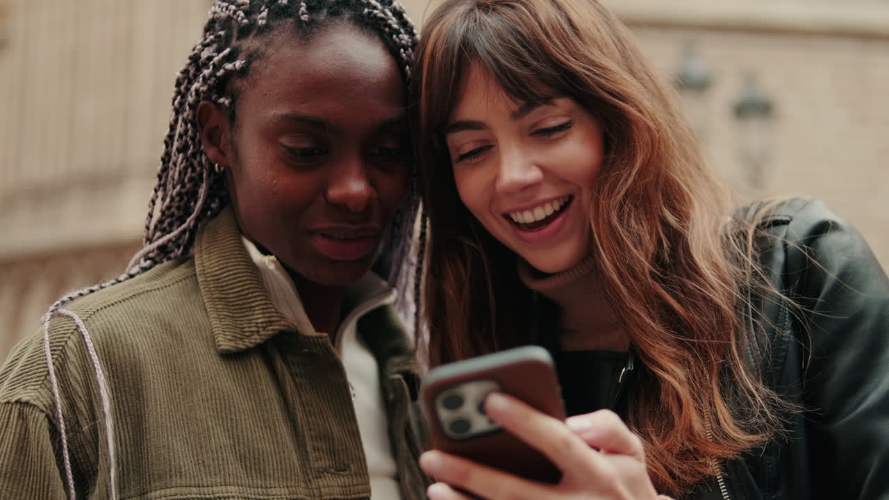 Due giovani donne diverse che sorridono e guardano lo smartphone
