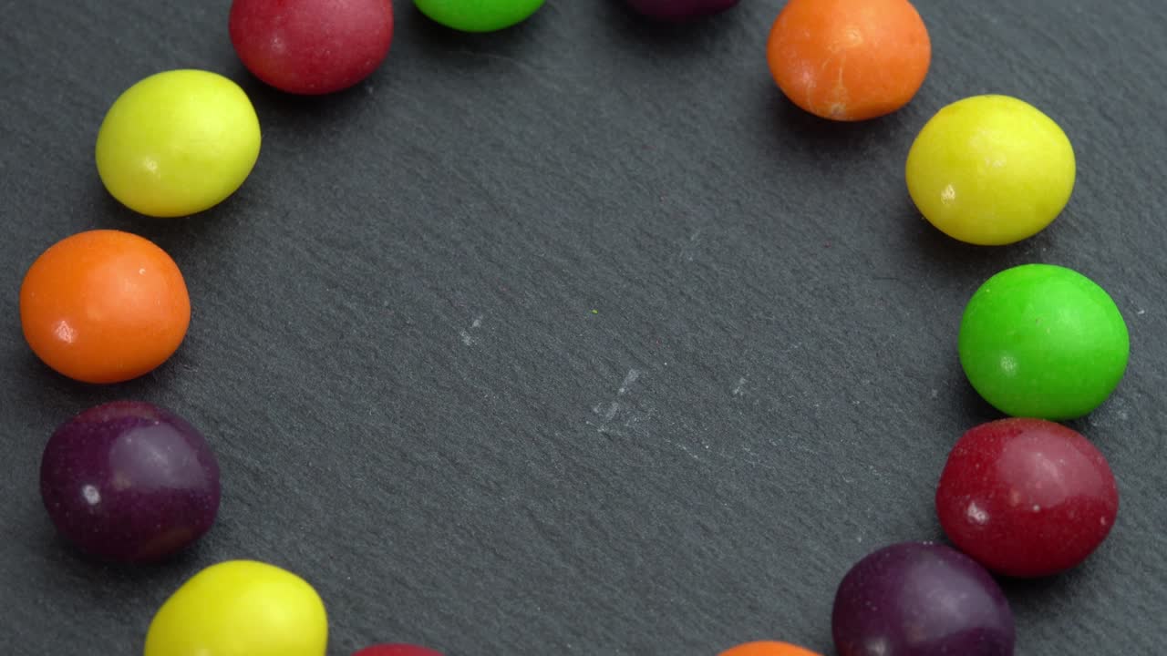 los dulces de colores giran sobre un fondo negro y la mano toma un dulce, dulces de color