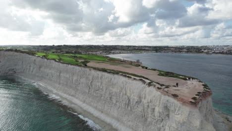 Vista-De-Pájaro-Sobre-El-Acantilado-De-Piedra-Caliza-Ras-Il--Fenek,-Con-Agua-Turquesa-Tropical,-Cielo-Azul-Y-Nubes-Blancas-Esponjosas,-Malta