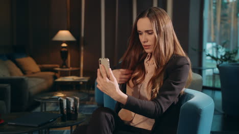 Business-woman-examining-face-makeup-looking-at-smartphone-in-cafe