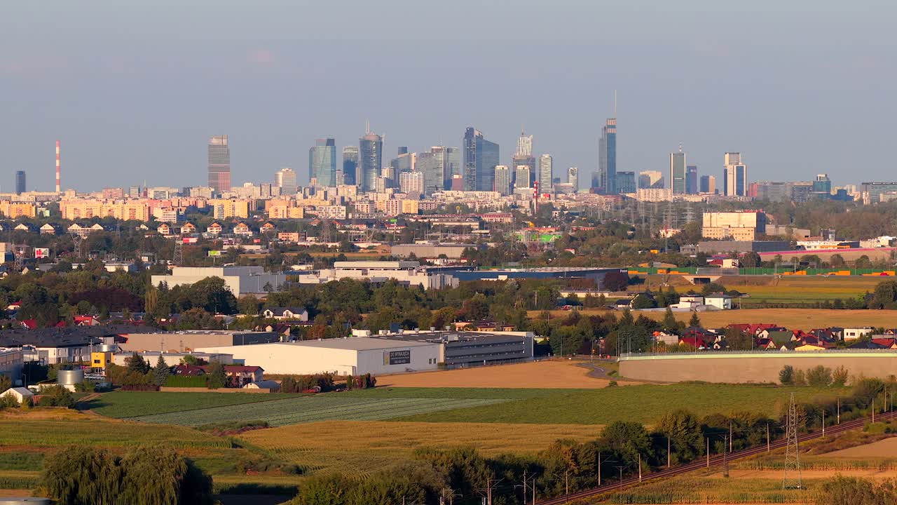 Skyline of Warsaw city in Poland at golden hour. Aerial panorama view. Industrial warehouses in foreground. View from suburb district. Wide shot. Farm fields and apartment blocks