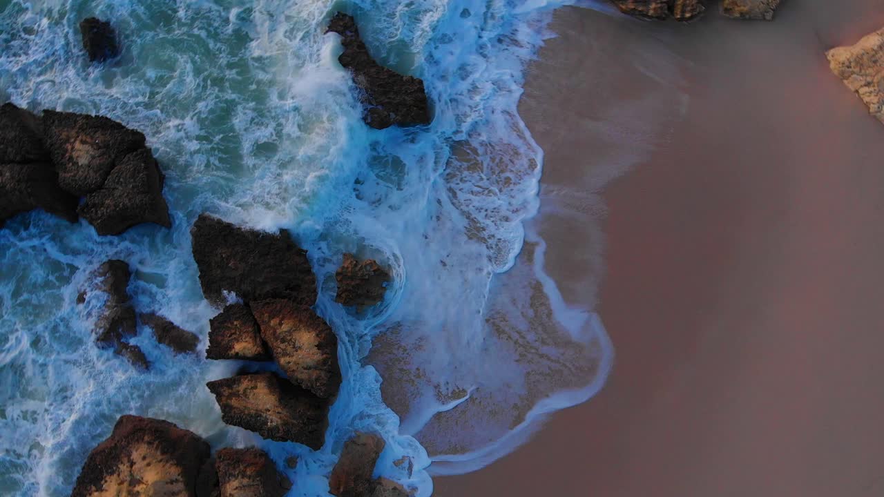 Beautiful aerial drone overhead rotating shot of waves crashing the rocky beach shore