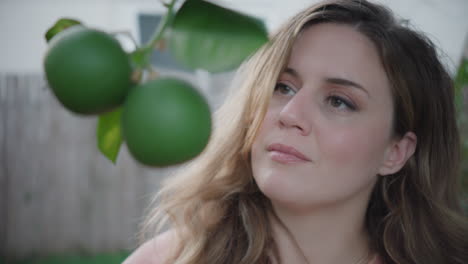 brown eyed woman admiring citrus plant growing on tree in backyard, daytime shot outside