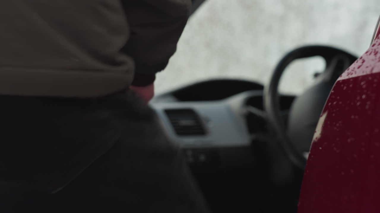 Close up of driver hand gripping chrome door handle to open red car covered with water droplets from snowfall, capturing realistic winter weather details and daily urban moment in cold environment