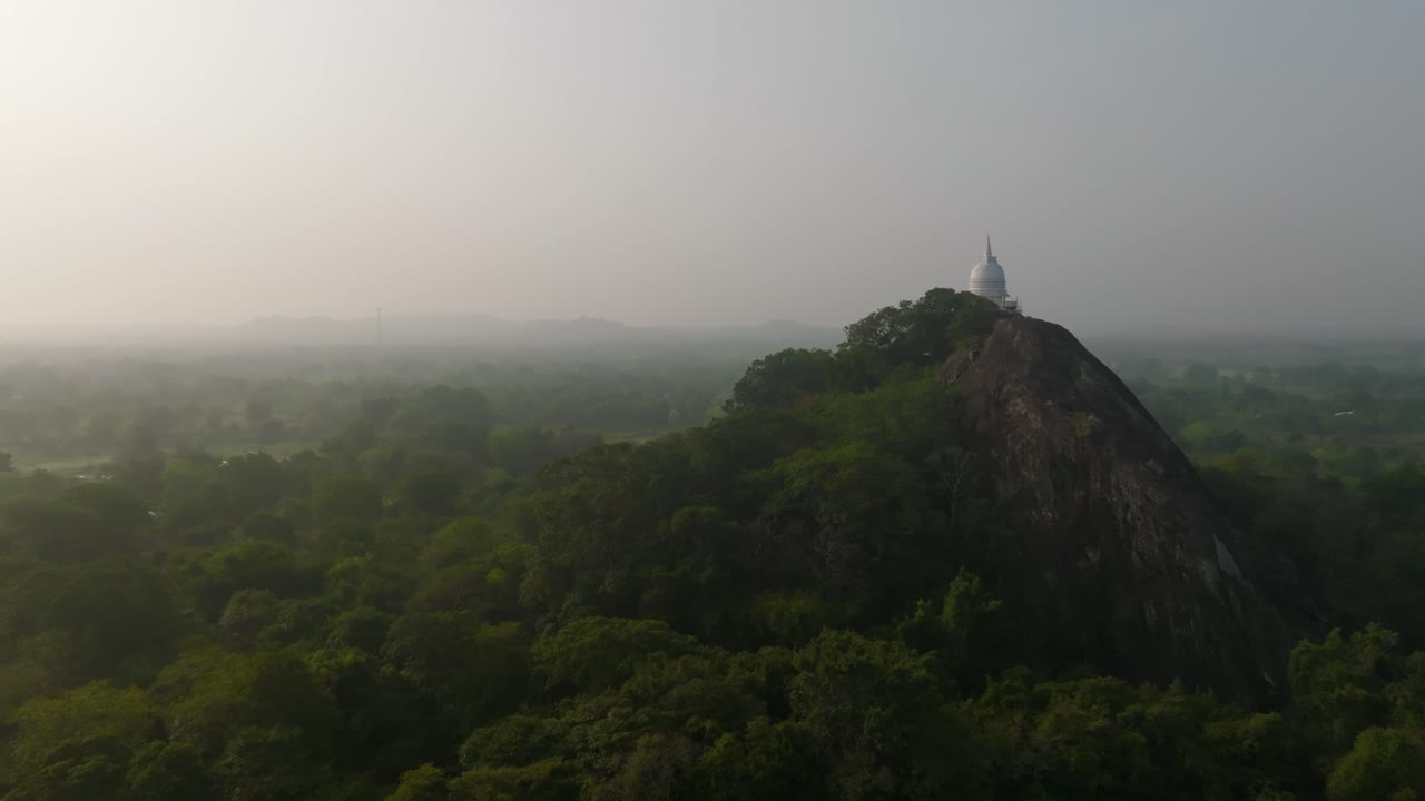 Vista laterale di un tempio a cupola bianca che corona una roccia frastagliata con la giungla sottostante in Sri Lanka