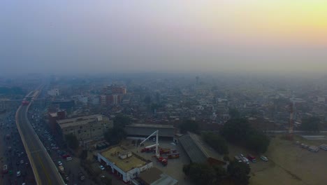 Vuelo-Aéreo-Sobre-La-Ciudad-Urbana,-Bombay,-India,-Vista-Superior,-Cruzando-Un-Puente-De-Autobús-De-Metro-Y-Una-Carretera,-Dos-Autobuses-De-Metro-En-Su-Puente-Pasando,-Una-Vista-Superior-Del-Centro-De-Rescate-De-Incendios