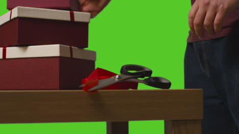 close up of man picking up gift wrapped presents in boxes decorated with ribbon on table shot against green screen