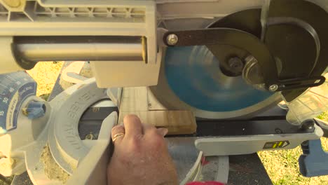 Man using miter saw to cut through wood for a project on a sunny day