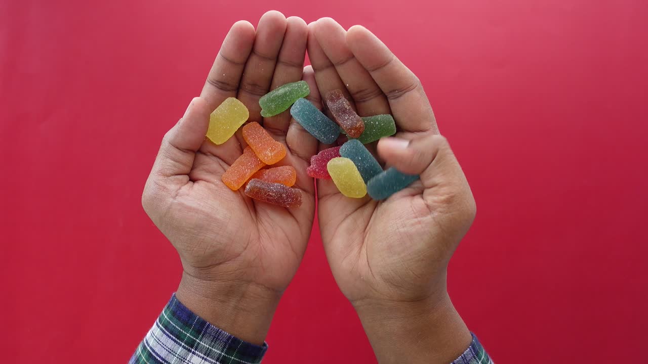 manos sosteniendo caramelos de jalea coloridos en un fondo rojo