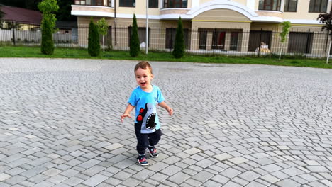 healthy active baby boy runs by the paved street. cute kid in t-shirt and pants is on the walk in summer.