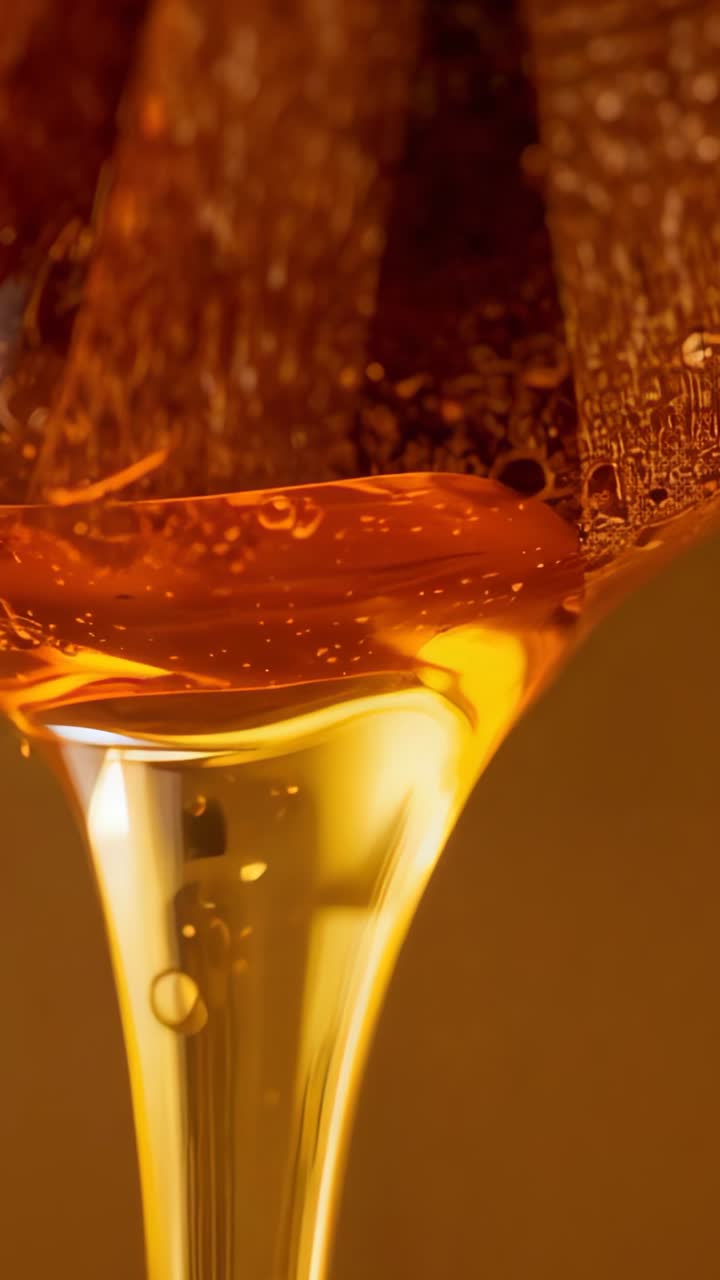 Vertical video: Releasing droplet from dipper sending honey flowing into glass container in kitchen