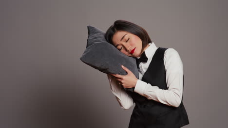 asian front desk staff falling asleep with pillow in hand