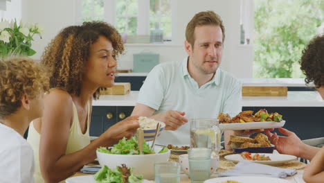 multi-racial family sitting around table in kitchen at home eating meal together