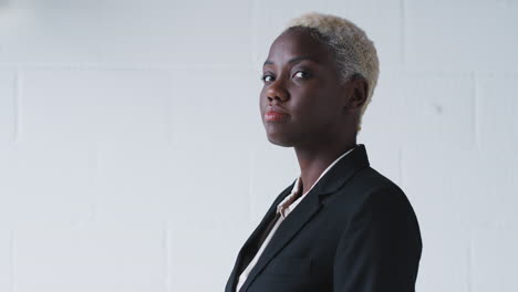 Portrait-Of-Smiling-Young-Businesswoman-Wearing-Suit-Standing-Against-White-Studio-Wall