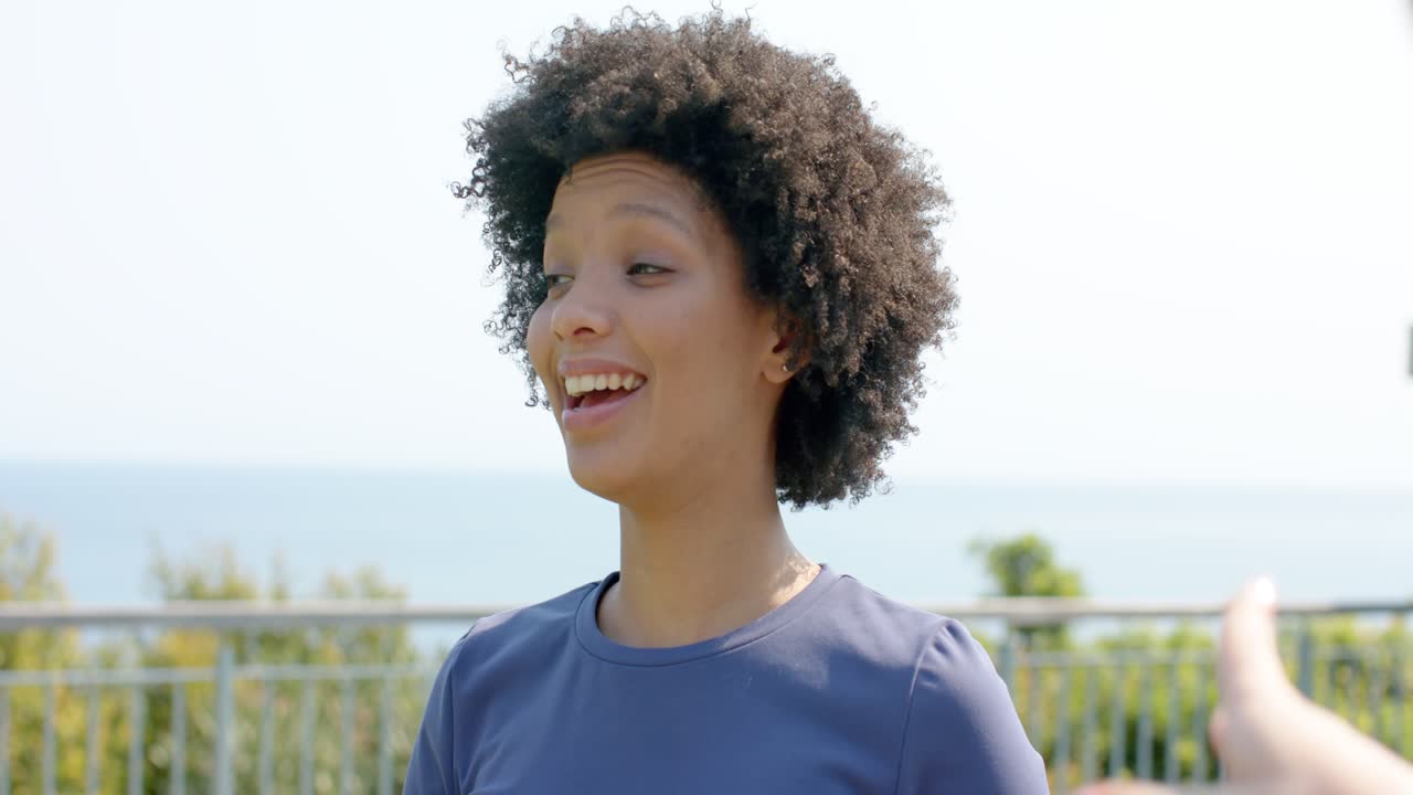 African American woman gesturing placing hands on chest on waterfront reacting to offscreen comment