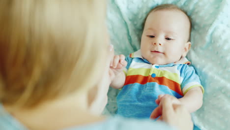 mom plays with the baby a boy of two months on the bed rear view shoulder woman